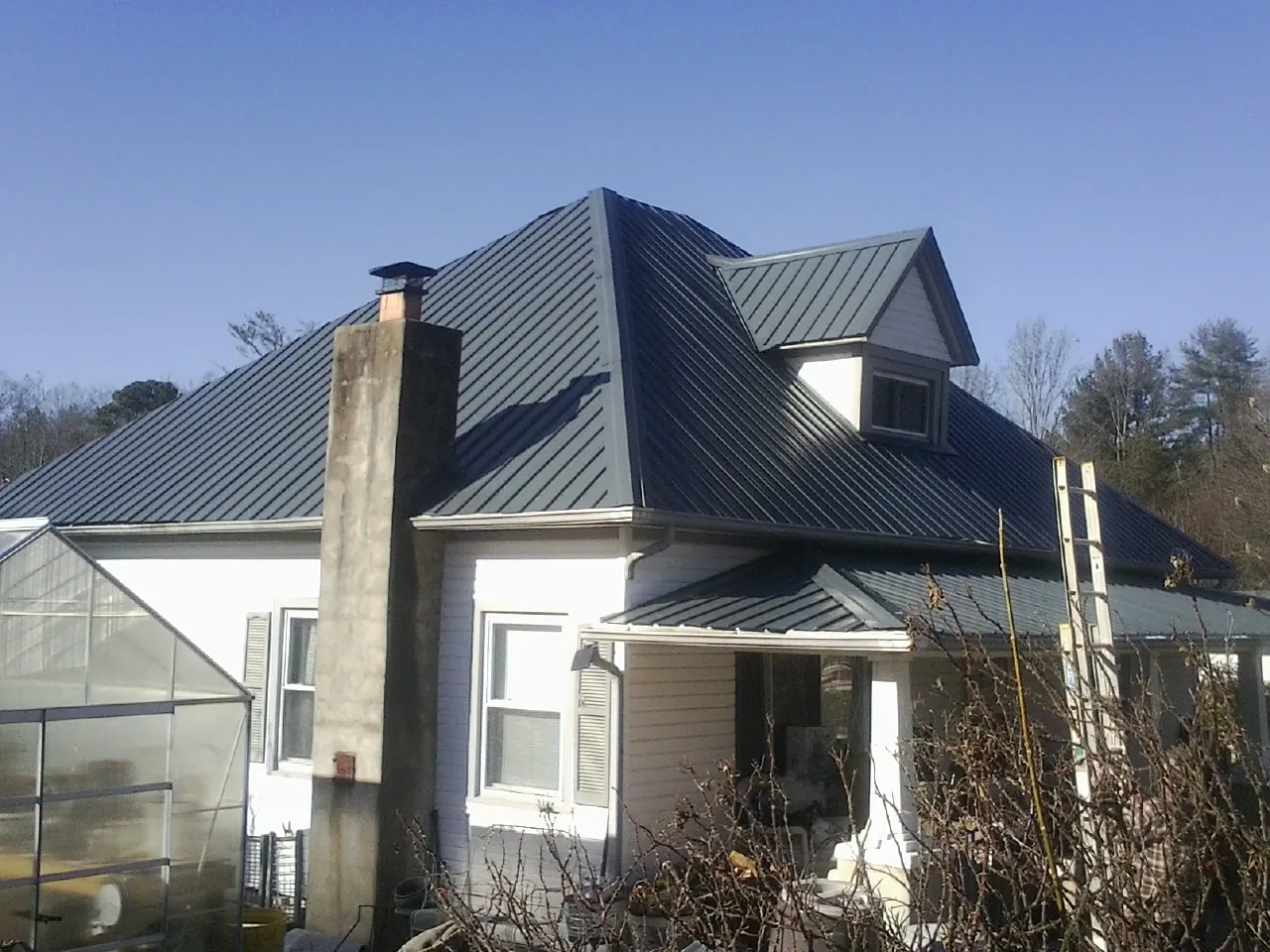 Dark blue standing seam metal roof on a white farmhouse with dormer — Slate & Tile Roof Repair by Roofing Brothers in Barnhart