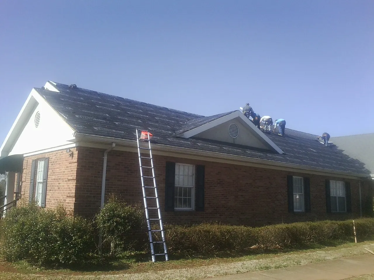 Crew tearing shingles off a brick ranch roof with a ladder set — Metal Roof Repair work by our crew in Barnhart