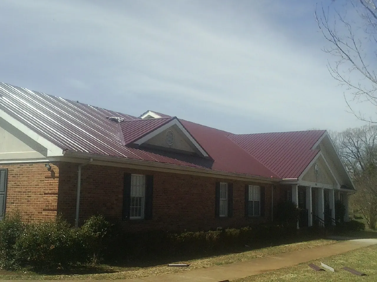 Red metal roof with gabled entries on a long brick building, from a Hail Damage Roof Repair job in Barnhart
