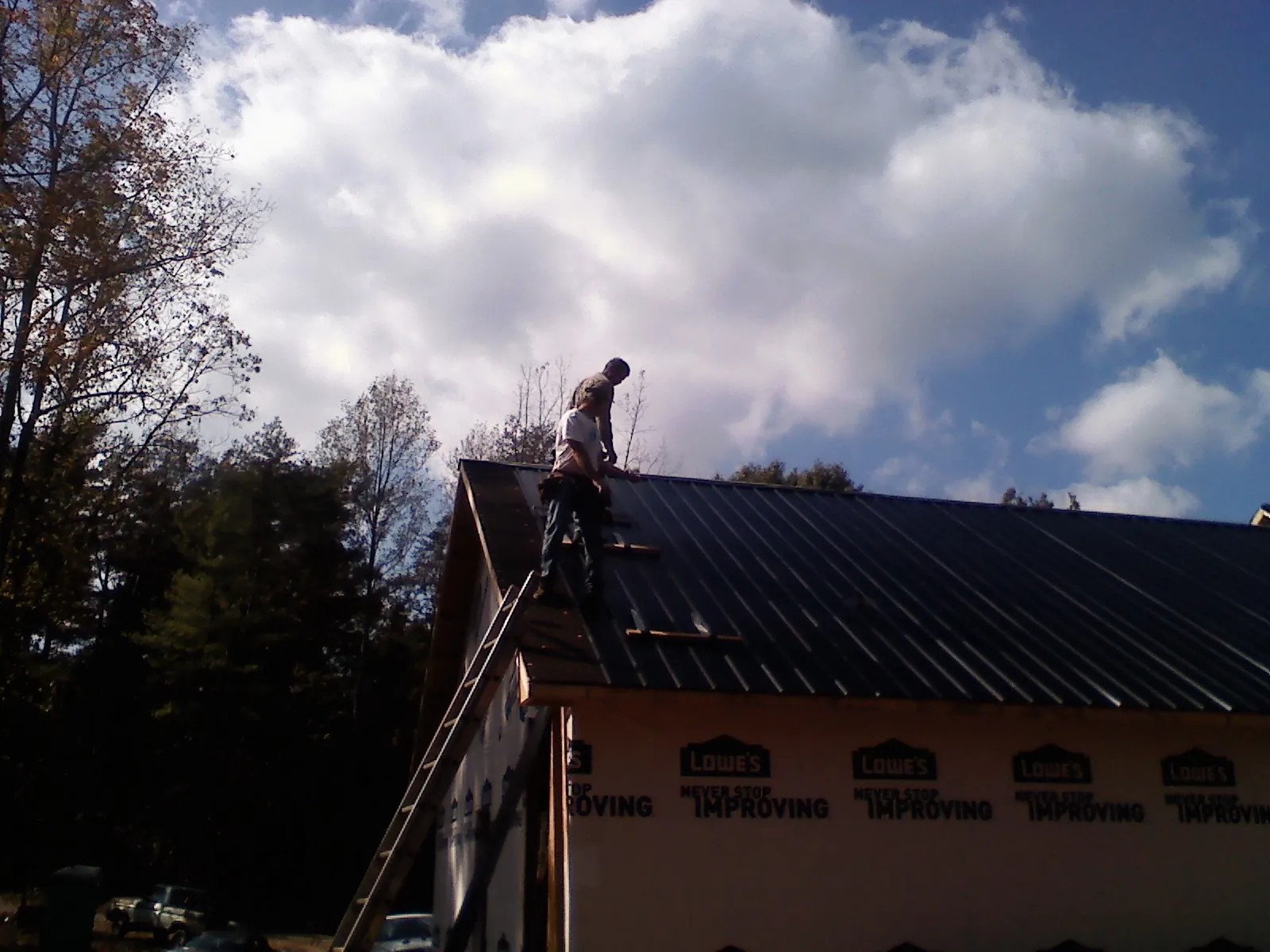 Roofer fastening dark metal panels high against a cloudy sky, from a Roof Inspection job in Barnhart