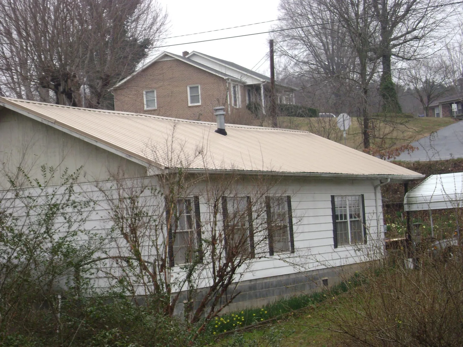 Tan metal roof on a white sided house set into a hillside — Commercial Roofing by Roofing Brothers in Barnhart