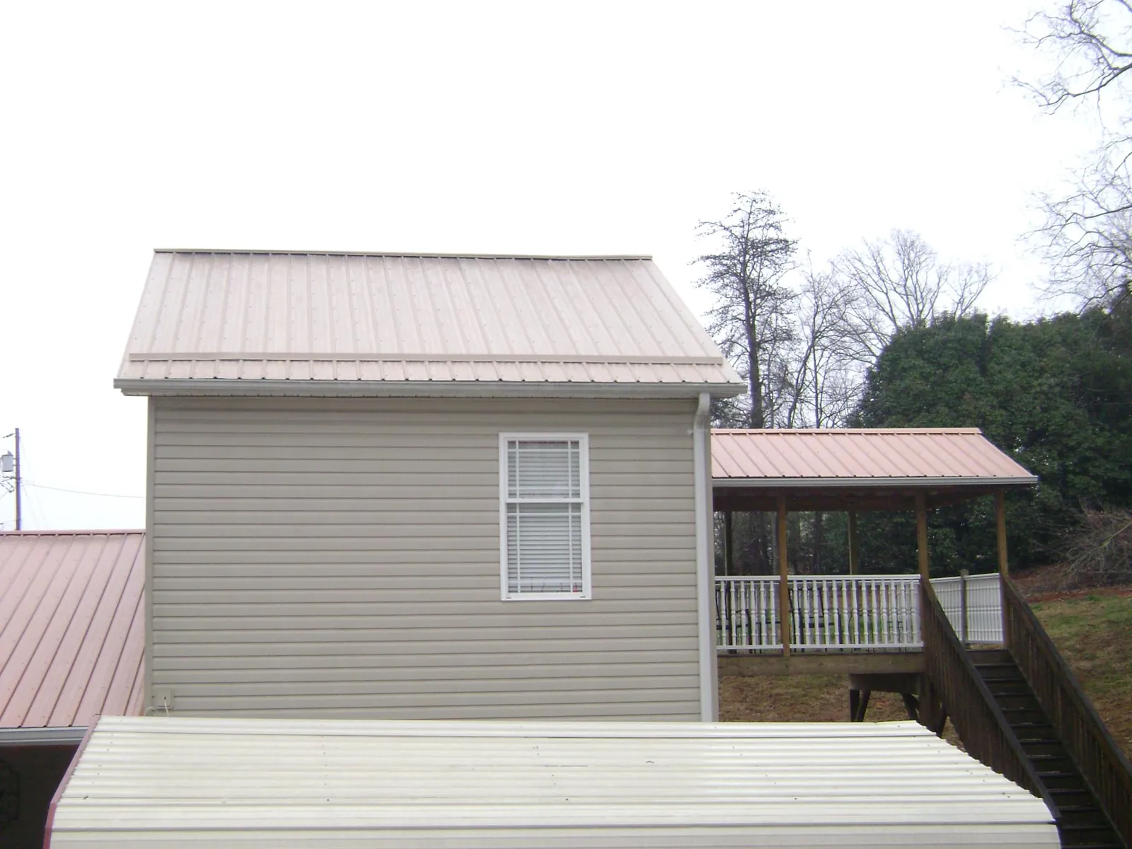 Tan metal roofs on a two story addition and attached porch, from a Roof Replacement job in Barnhart